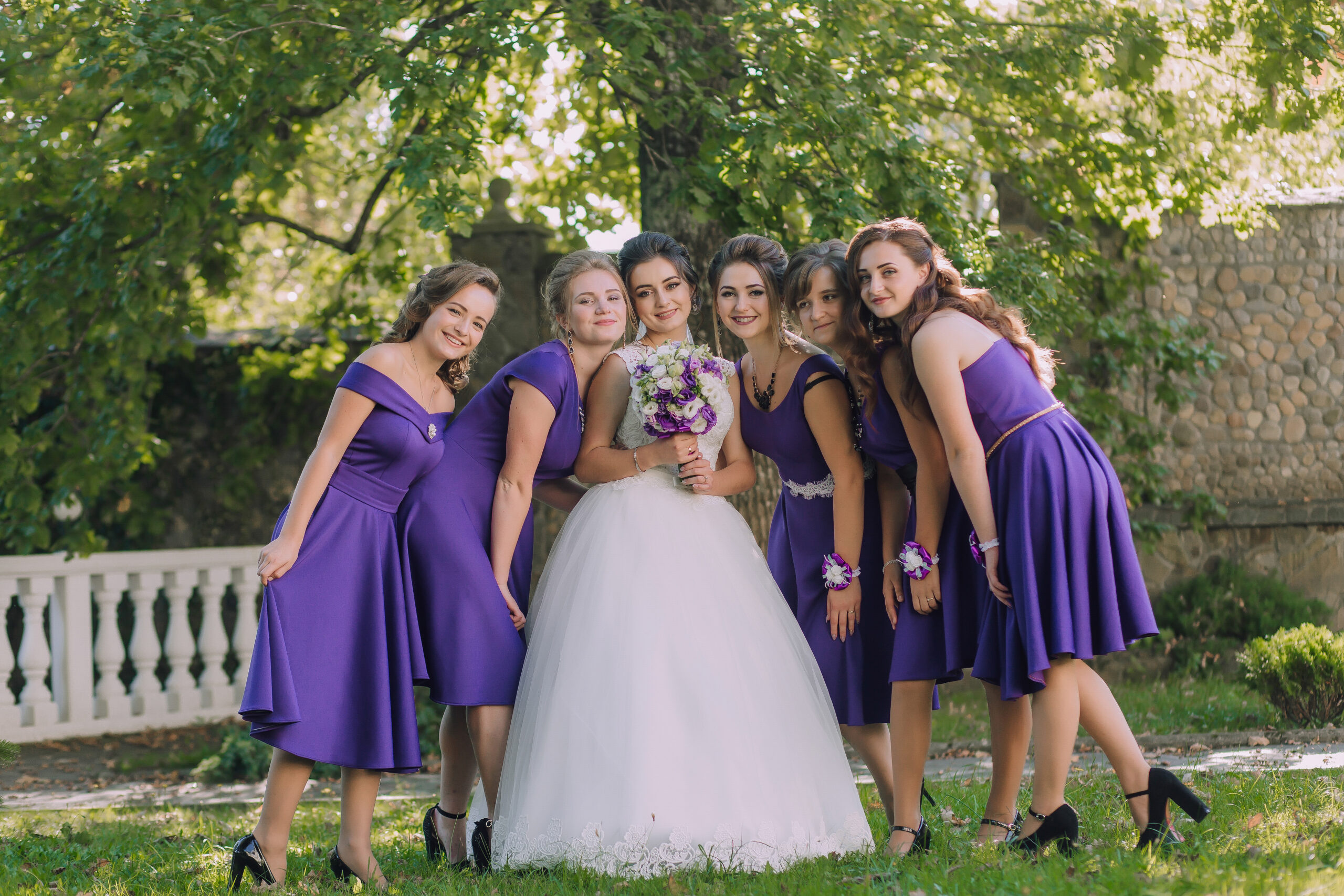 Bride in white surrounded by 4 young bridesmaids in purple dresses